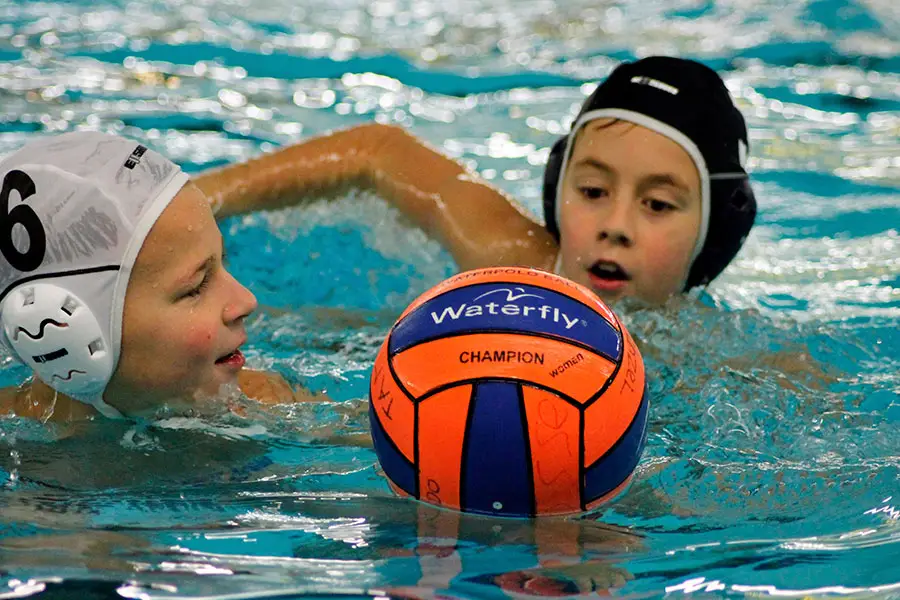 Twee kinderen met badmuts en een oranje-blauwe bal, close-up in het water